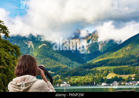 Blick auf die Landschaft rund um den Hallstätter See mit Bergen, Wald und blauer Himmel mit Wolken. Eine junge Frau wird mit einer Kamera fotografieren. Stockfoto