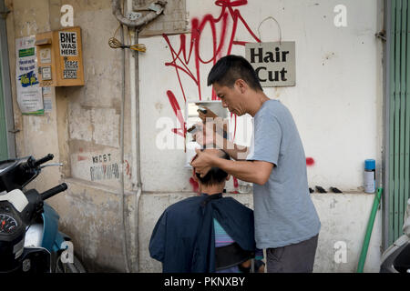 Ein Friseur Haare schneiden für seine Kunden auf der Straße in der Altstadt von Hanoi, Vietnam Stockfoto