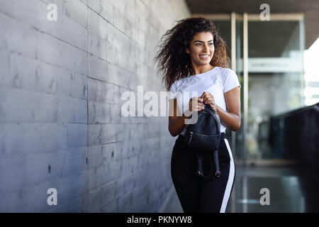 Junge afrikanische Frau mit schwarzen Locken Frisur zu Fuß in der Nähe von Business Gebäude. Gerne Arabische Mädchen im Sport Kleidung auf der Straße. Stockfoto