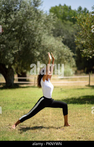 Junge arabische Frau Yoga in der Natur. Afrikanische Frauen tragen sportliche Kleidung tun Krieger Abbildung im städtischen Park. Stockfoto