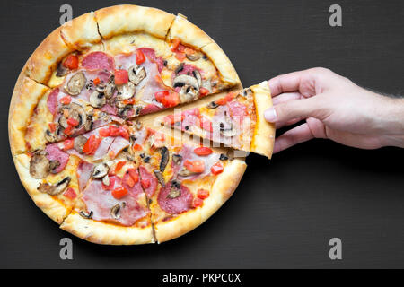 Der Mann nimmt Scheibe frisch gebackene Pizza, Ansicht von oben. Overhead, von oben. Close-up. Schwarzen Hintergrund. Stockfoto