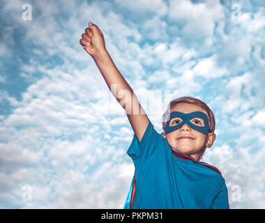 Porträt eines kleinen Jungen tragen Kostüm von Superhelden mit einer Hand über Himmel Hintergrund aufgewachsen, bereitet sich darauf vor, die Welt zu retten, Kid spielt Superman Stockfoto