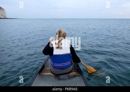 Die Rückseite Blick auf eine 60 Jahre alte Frau sitzt vorne in einem Kajak paddeln mit einem Paddel aus Holz trägt sie eine Schwimmweste und hat blonde Haare Stockfoto