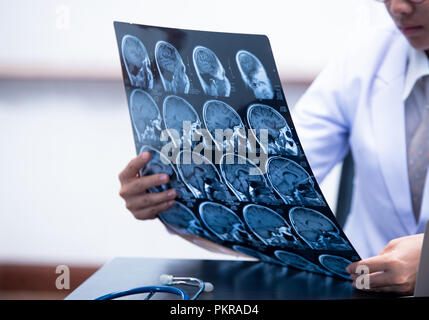 Junge Ärztin holding MRI oder CT-Bild, Arzt in Uniform sitzen im Arbeitsraum und Holding X-ray Bild für Diagnose Hirnverletzung oder Scannen Stockfoto