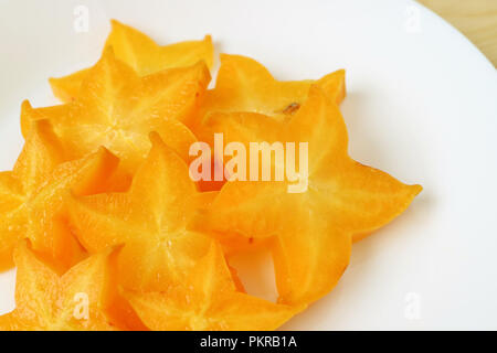 Blick von oben auf die leuchtend orange-gelbe Farbe frische reife Star Fruit in vielen Stücken auf einem weißen Teller geschnitten Stockfoto