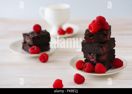 Himbeere brownies auf weißem Porzellan Teller mit Goldrand stack und mit frischen Beeren garniert. Porzellan Schale in Bokeh, weiß Holz- Hintergrund, h Stockfoto