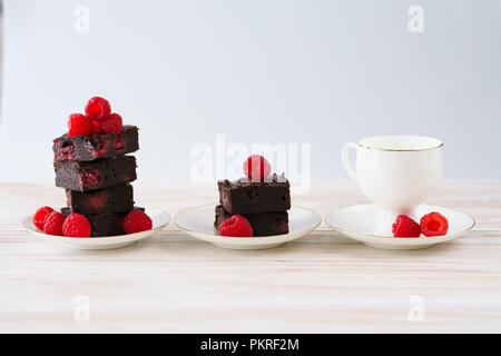 Himbeere brownies auf weißem Porzellan Teller mit Goldrand stack und mit frischen Beeren garniert. Weiß Holz- Hintergrund, hohe Auflösung. Stockfoto