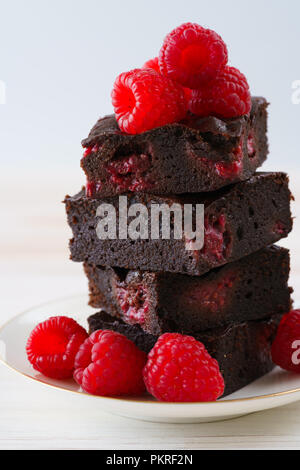 Himbeere brownies auf weißem Porzellan Teller mit Goldrand stack und mit frischen Beeren garniert. Weiß Holz- Hintergrund, hohe Auflösung. Stockfoto