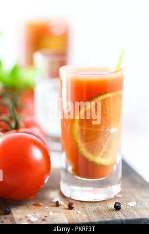 Sangrita in einem Glas serviert mit frischen Tomaten, selleriestangen und schwarzem Pfeffer. Tequila Flasche in Bokeh, Holzbrett, hohe Auflösung. Stockfoto