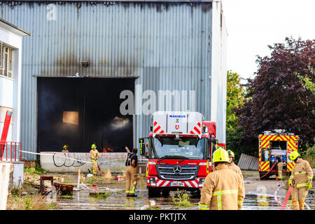 Löschfahrzeuge und Crew an factory Brand in Lagerhalle am Cummins Fabrik, Westwood, Margate. Zwei Motoren mit Feuerwehrleuten geparkt. Rauch Lager mit kleinen Flammen in. Stockfoto