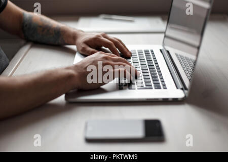 Mann, der an einem Notebook arbeitet. Grafiktablett, Handy und ein Laptop auf einem Holztisch Stockfoto