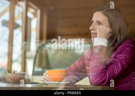 Profil anzeigen von eine junge Frau sitzt in einer Bar alleine Kaffee trinken und ihr Kopf lehnte sich auf ihre Hand. Stockfoto