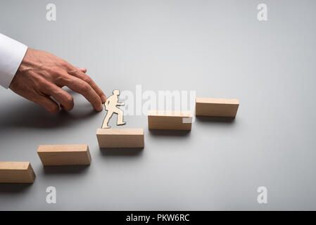 Geschäftsmann, klettern Sie die Schritte zum Erfolg und Fortschritt in einem konzeptionellen Bild mit Papier silhouette Ausschnitt aus einem Mann und einer männlichen Hand helfen ihm c Stockfoto