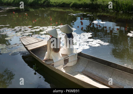 Zwei charmante Vietnamesische Mädchen in traditionellen weißen langen kleid sitzen auf dem Boot an Thanh Thuy Dorf in Hue, Vietnam Stockfoto