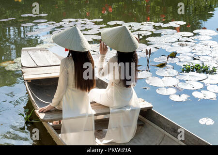 Zwei charmante Vietnamesische Mädchen in traditionellen weißen langen kleid sitzen auf dem Boot an Thanh Thuy Dorf in Hue, Vietnam Stockfoto