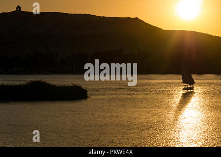 Silhouette von traditionellen Feluke Segelboot mit orange Sonne über Hügel Silhouette, der Nil, Assuan, Ägypten, Afrika Stockfoto