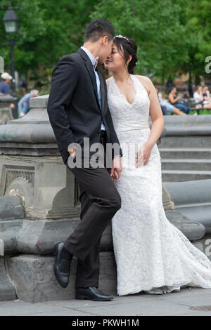 Eine Asiatische amerikanisches Paar für Fotos in der Nähe der Brunnen im Washington Square Park in Manhattan, New York City darstellen. Stockfoto