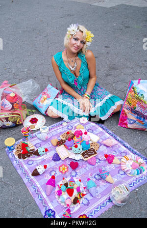 Eine schöne junge Frau, die von Hand stricken Repliken von Speisen und Desserts verkauft. Im Union Square Park in Manhattan, New York City. Stockfoto