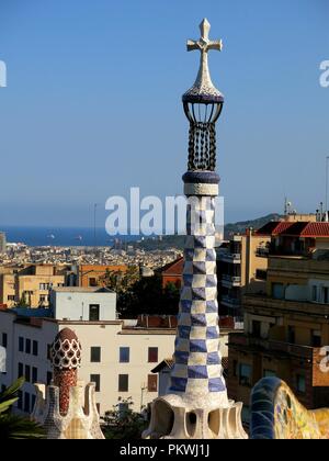 Turm und Blick auf die Stadt von Barcelona vom Park Güell. Im Vordergrund Turm mit einem Kreuz vom Gebäude am Eingang des Parks. Stockfoto