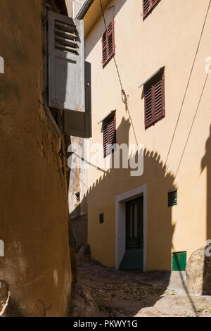 Schmale Straße mit alten ebnet. Fenster mit Fensterläden. Schatten von einem gegenüberliegenden Haus an der Wand. Nach Abzug der elektrischen Leitungen. Stadt Crikvenica, Insel Krk, Croati Stockfoto