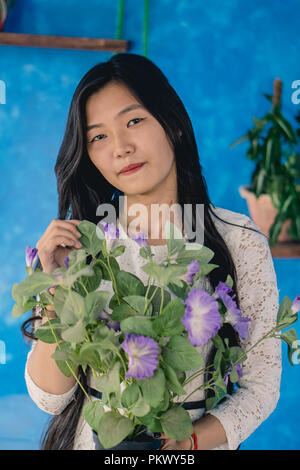 Mädchen, dass ein Topf von Violett petunie vor einem blauen Hintergrund. Stockfoto