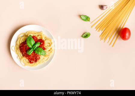 Spaghetti Spaghetti Bolognese und Zutaten auf rosa Hintergrund, Ansicht von oben. Teller Pasta mit Tomatensauce und Basilikum auf kreative gelben Hintergrund. Stockfoto