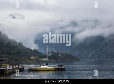 Kleines Boot an einem nebligen ruhigen See mit Bergen im Hintergrund Stockfoto