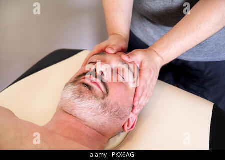 Mann, Behandlung für sein Angesicht zu Massagetisch, Medizin Konzept. Masseur massieren bemannt Gesicht. Schöner Mann entspannende Gesichtsmassage empfangen. Stockfoto
