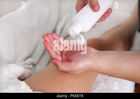 Massage studio entspannen. Männer Hände Flasche Massageöl. Körperpflege. Schöne Frau auf einem Massagetisch ist in seinen unteren Rücken durch einen Masseur massiert setzen Stockfoto