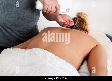 Massage studio entspannen. Männer Hände Flasche Massageöl. Körperpflege. Schöne Frau auf einem Massagetisch ist in seinen unteren Rücken durch einen Masseur massiert setzen Stockfoto