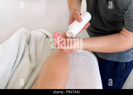 Massage studio entspannen. Männer Hände Flasche Massageöl. Körperpflege. Schöne Frau auf einem Massagetisch ist in seinen unteren Rücken durch einen Masseur massiert setzen Stockfoto