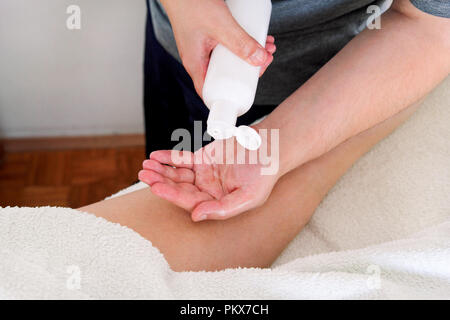 Massage studio entspannen. Männer Hände Flasche Massageöl. Körperpflege. Schöne Frau auf einem Massagetisch ist in seinen unteren Rücken durch einen Masseur massiert setzen Stockfoto