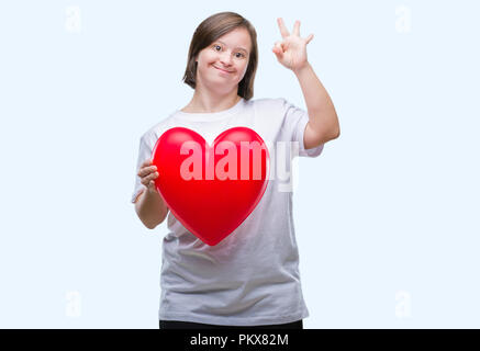 Junge erwachsene Frau mit Down Syndrom halten roten Herzen über isolierte Hintergrund tun ok Zeichen mit den Fingern, ausgezeichnete Symbol Stockfoto