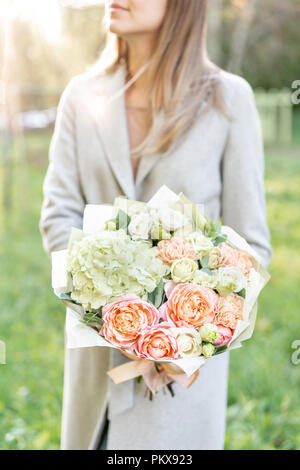 Close-up schöner Frühling Blumenstrauß in den Händen. zarte Blume Anordnung mit rosa und grünen Pastelltönen Blumen. Rasen im Hintergrund. Helle Sonnenaufgang oder Sonnenuntergang Sonne. Stockfoto