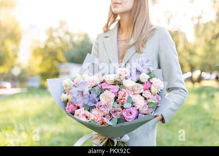 Lila und rosa Pastell schöner Frühling Bouquet. Junges Mädchen hält ein Blumenarrangement mit verschiedenen Blumen. Helle Sonnenaufgang oder Sonnenuntergang Sonne Stockfoto