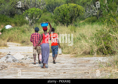 Afrikanische Frau wandern die Becken auf dem Kopf und zwei junge Männer wandern, Afrika Frau trägt Last auf dem Kopf, Uganda Stockfoto