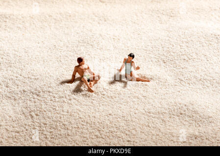 Paar miniatur Menschen entspannend an einem Sandstrand in einem konzeptionellen Bild von Sommer Ferien, Entspannung und dating Stockfoto