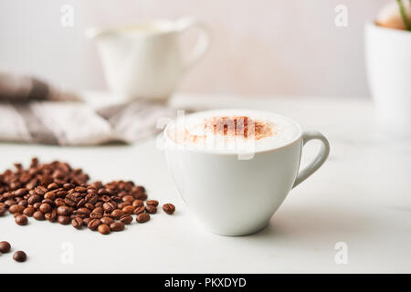 Cappuccino in einem weißen Keramik Kaffeetasse mit gerösteten Kaffeebohnen. Feminine rose Hintergrund mit kopieren. Bild mit hoher Auflösung, schmale tiefe der f Stockfoto