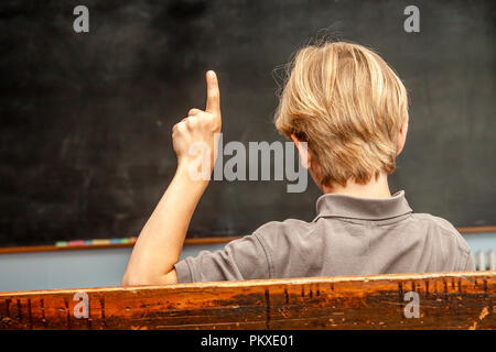 Begriff der öffentlichen Grundschule mit Jungen seine Hand heben im Klassenzimmer. Stockfoto