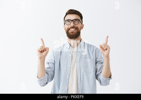 Taille - geschossen von Verträumten kreative und stattlichen männlichen Modell in Schwarz Computer Gläser und Modisches Shirt heben die Hände suchen und zeigt mit Freude Freude Ausdruck über grauer Hintergrund Stockfoto
