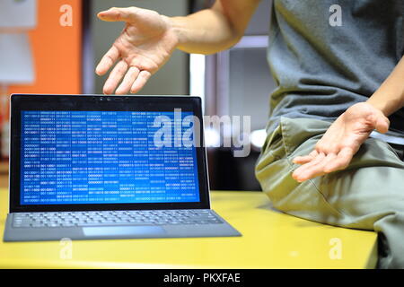 Computer coding Präsentation auf dem Bildschirm. Mock up Blau binäre Anzeige auf Laptop monitor Notebook auf dem Tisch und die Hände in Richtung in einem invi Stockfoto