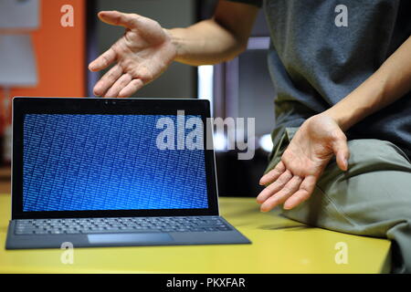 Computer coding Präsentation auf dem Bildschirm. Mock up Blau binäre Anzeige auf Laptop monitor Notebook auf dem Tisch und die Hände in Richtung in einem invi Stockfoto