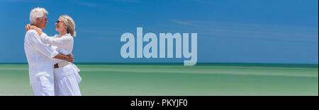Panorama banner Bild eines glücklichen älterer Mann und Frau Paar zusammen, die durch das Meer auf einer einsamen tropischen Strand mit hellen blauen Himmel Stockfoto