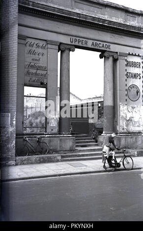 1950, historische, Mann mit seinem Fahrrad und Tochter an den Ruinen der Säulen vor dem Eingang des Oberen Arcade in Broadmead, Bristol, England, die schlecht während der Blitz im Zweiten Weltkrieg bombardiert wurde. Beachten Sie das Fehlen des Eisernen Geländer, am Eingang, die nach der Bombardierung für den Einsatz im Krieg - Zeit Fabriken entfernt wurden. Nach dem Krieg wurde die obere Arcade wurde nie wieder aufgebaut, aber glücklicherweise der unteren Arcade wurde, nachdem im Jahr 1949 verzeichnet worden. Stockfoto