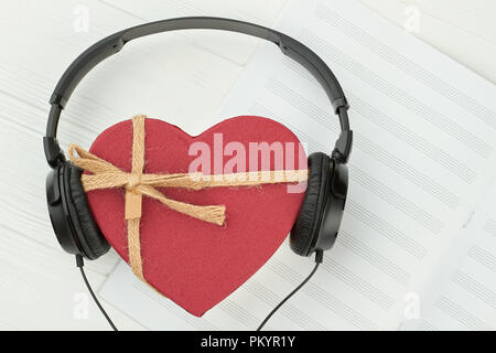 Roter Geschenkbox und schwarz Kopfhörer. Kopfhörer mit Herzförmigen Geschenkbox auf musikalische Note. Liebe Musik Konzept. Stockfoto