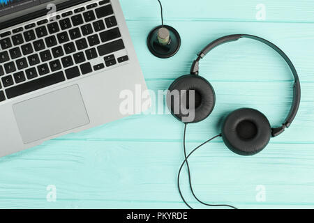 Laptop und Kopfhörer auf blauem Hintergrund. Tragbarer Laptop mit Headset und Mini Stereo Mikrofon auf farbigen Holz- Hintergrund. Moderne Geräte Konzept Stockfoto