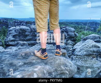 Wanderer Mann einen Rest am Berg. Männliche Beine auf scharfen Gipfel und Wanderer genießen Sie die spektakuläre Aussicht. Stockfoto