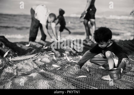 Kind sammelt Fisch im Netz und stellt sie in einen kleinen Eimer. Retro Style Schwarz/Weiß-Fotografie Stockfoto