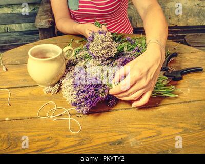 Mädchen Hände mit Schere und string Vorbereitung Lavendelblüten Trauben auf hölzernen Tisch. Stockfoto