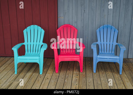 Drei Aquamarin, roten und blauen Plastikadirondack Stühle auf einem Holzdeck Stockfoto